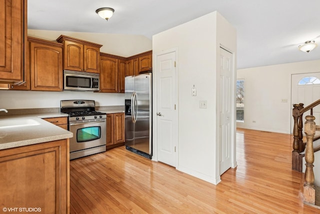 kitchen featuring vaulted ceiling, stainless steel appliances, light hardwood / wood-style floors, and sink