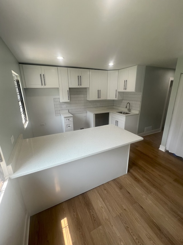 kitchen featuring white cabinetry, wood-type flooring, sink, and decorative backsplash