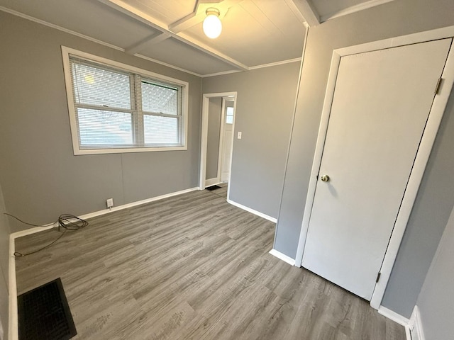 unfurnished bedroom featuring coffered ceiling, crown molding, wood-type flooring, and beam ceiling