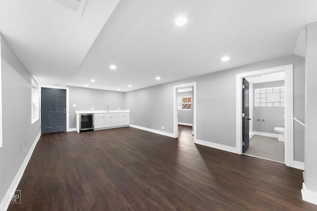 unfurnished living room with wine cooler, dark wood-type flooring, and bar area