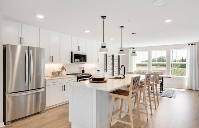 kitchen featuring white cabinetry, a kitchen island with sink, stainless steel appliances, hanging light fixtures, and sink