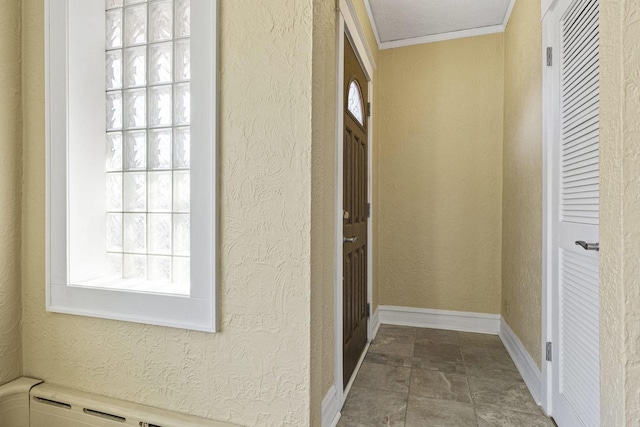hall featuring baseboards, a textured wall, ornamental molding, and stone finish flooring