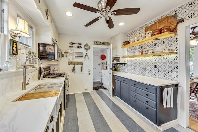 kitchen with sink, stainless steel range with gas stovetop, light stone countertops, white cabinets, and decorative backsplash