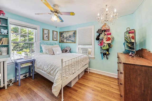 bedroom with hardwood / wood-style flooring, ceiling fan with notable chandelier, and cooling unit