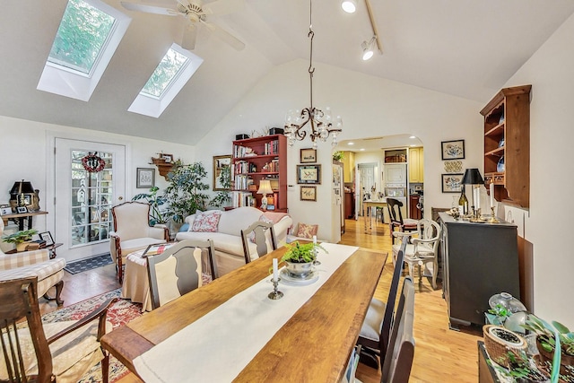 dining space with a wealth of natural light, ceiling fan with notable chandelier, high vaulted ceiling, and light hardwood / wood-style flooring