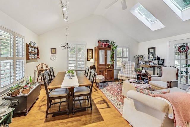 dining room with a skylight, high vaulted ceiling, ceiling fan, and light hardwood / wood-style flooring