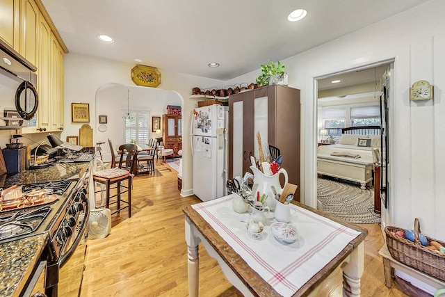 kitchen featuring white refrigerator, black gas range oven, light brown cabinets, and light wood-type flooring