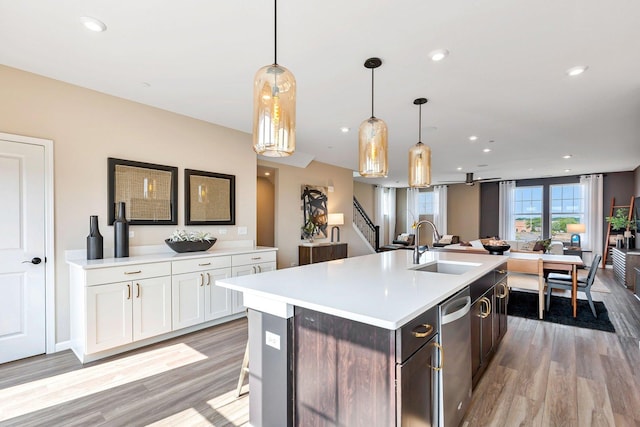 kitchen with sink, decorative light fixtures, light hardwood / wood-style floors, a kitchen island with sink, and white cabinets