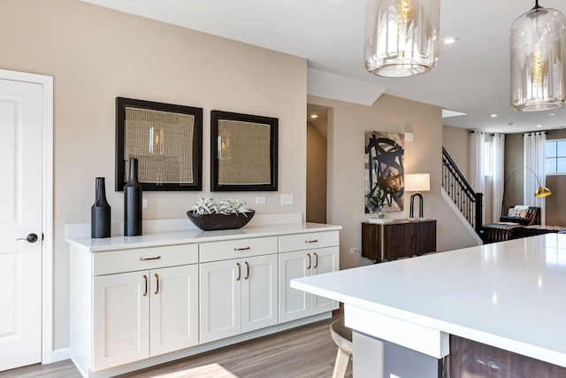 kitchen with decorative light fixtures, a kitchen breakfast bar, white cabinets, and light wood-type flooring