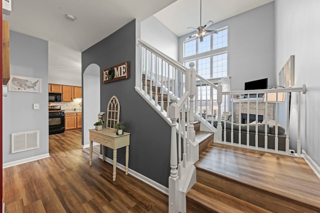 staircase featuring hardwood / wood-style floors, a towering ceiling, a fireplace, and ceiling fan