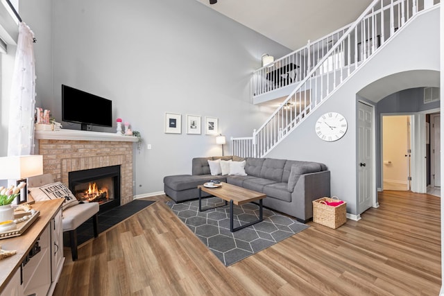 living room with hardwood / wood-style flooring, a brick fireplace, and a towering ceiling