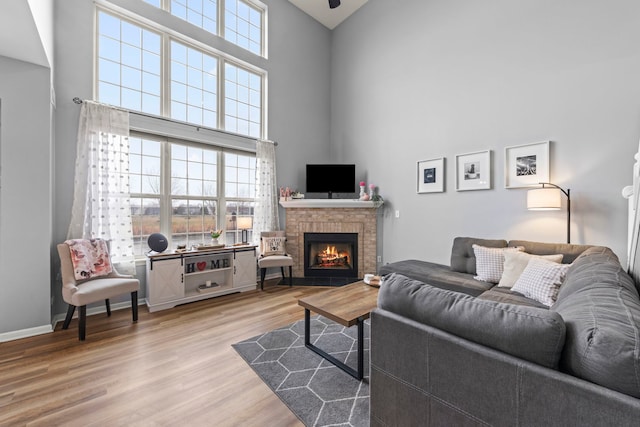 living room with light hardwood / wood-style floors, a brick fireplace, and a high ceiling