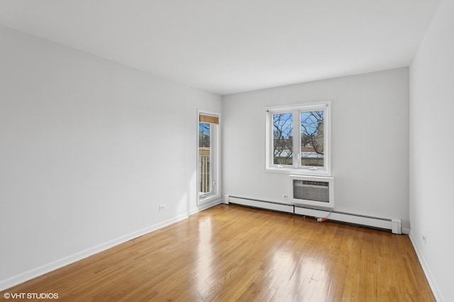 unfurnished room with baseboard heating, an AC wall unit, baseboards, and light wood-style floors