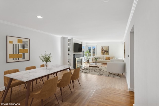 dining area featuring a tiled fireplace, recessed lighting, crown molding, and light wood-style floors