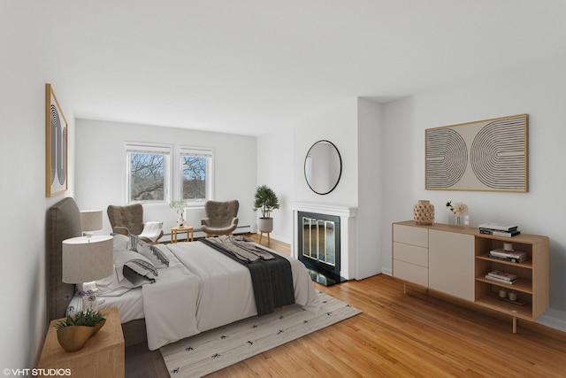 bedroom with a glass covered fireplace and wood finished floors