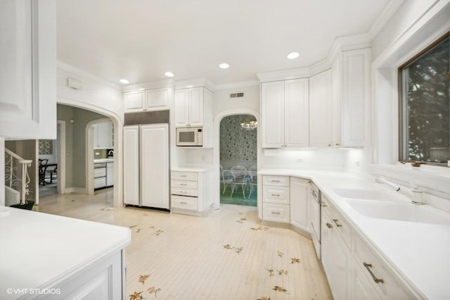 kitchen with white cabinetry, built in appliances, sink, and crown molding