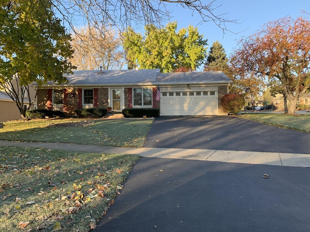 ranch-style house featuring aphalt driveway, an attached garage, brick siding, and a front yard