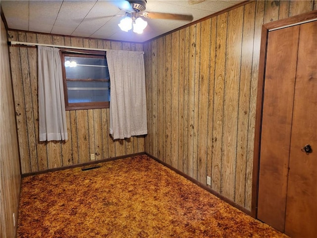 empty room featuring carpet floors, ceiling fan, and wood walls