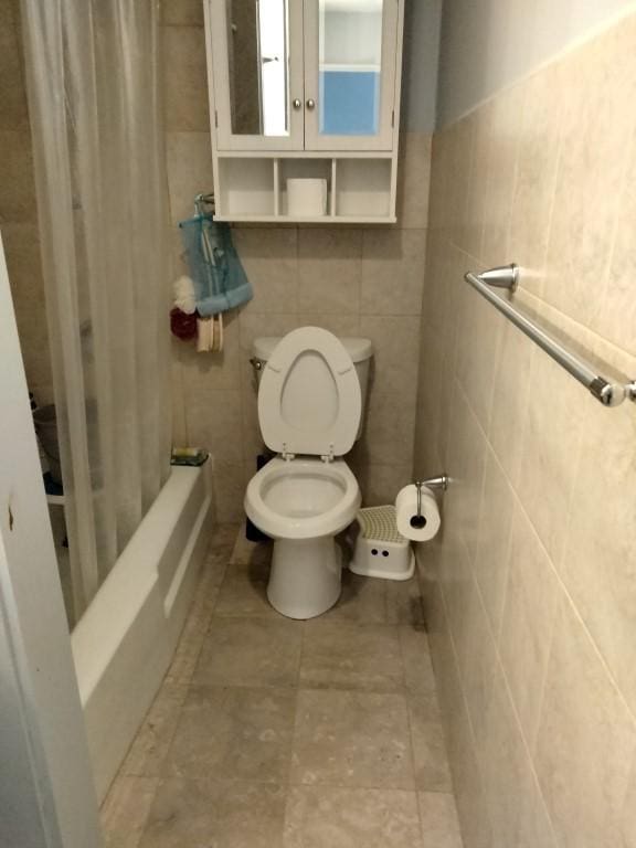 bathroom featuring tile walls, toilet, and shower / tub combo with curtain