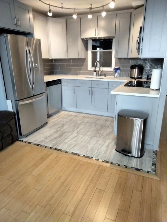 kitchen with stainless steel appliances, gray cabinets, light hardwood / wood-style flooring, and backsplash