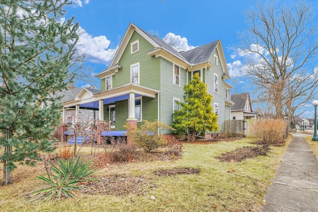 victorian house featuring a porch, a front yard, and fence