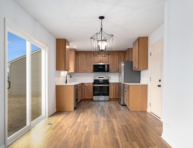 kitchen with pendant lighting, sink, hardwood / wood-style flooring, appliances with stainless steel finishes, and an inviting chandelier