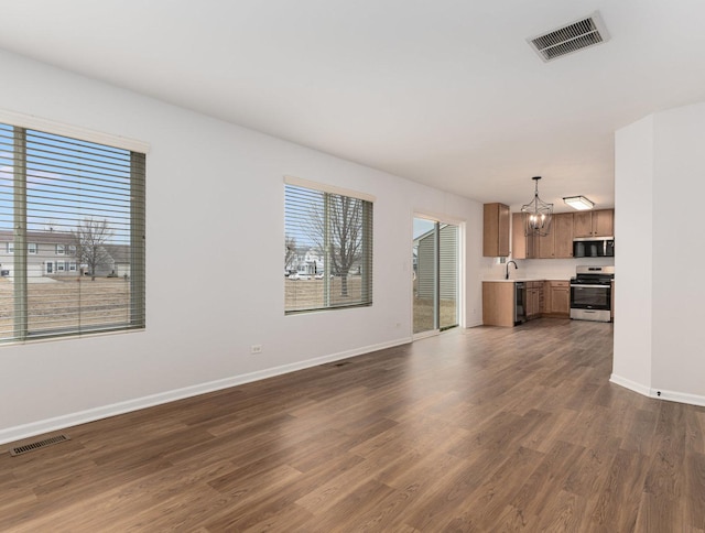 unfurnished living room with sink, a notable chandelier, and dark wood-type flooring