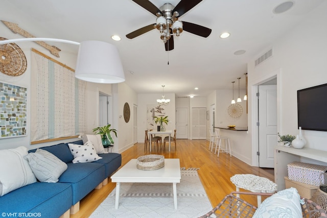 living room featuring ceiling fan with notable chandelier and light hardwood / wood-style flooring