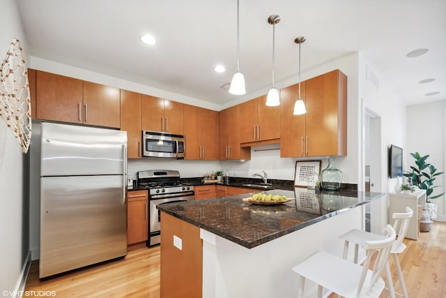 kitchen featuring a kitchen bar, sink, light wood-type flooring, pendant lighting, and stainless steel appliances