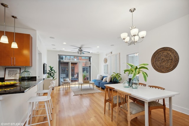 dining space with ceiling fan with notable chandelier and light hardwood / wood-style floors