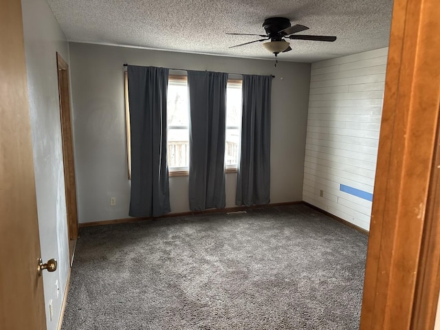 carpeted spare room with ceiling fan, a textured ceiling, and wood walls