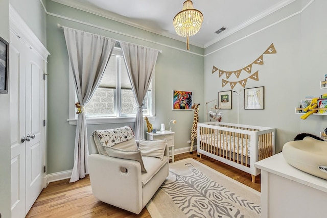 bedroom featuring a crib, ornamental molding, an inviting chandelier, and light hardwood / wood-style floors