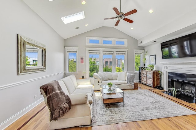 living room featuring hardwood / wood-style flooring, ceiling fan, a skylight, and high vaulted ceiling