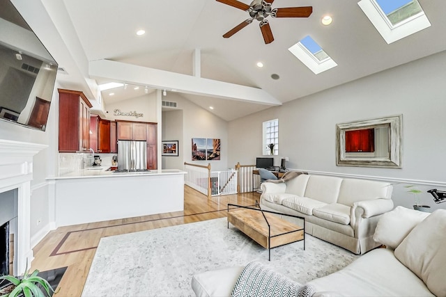 living room with high vaulted ceiling, a skylight, light hardwood / wood-style floors, and ceiling fan