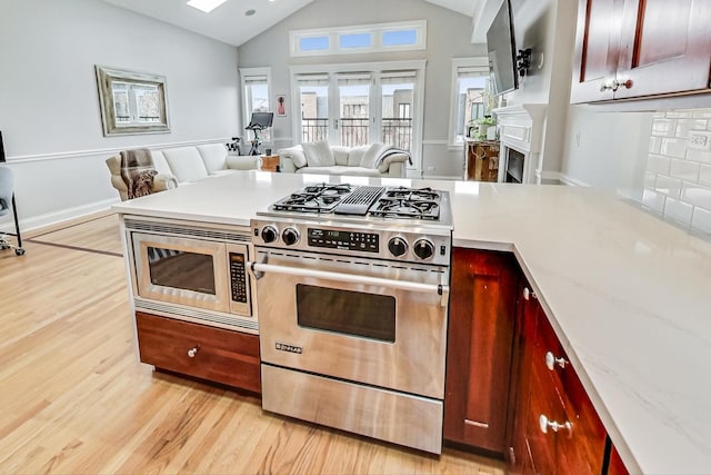 kitchen with light stone counters, appliances with stainless steel finishes, high vaulted ceiling, and light wood-type flooring