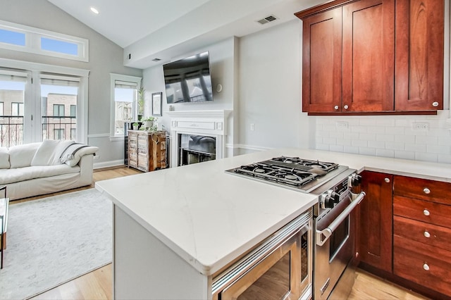 kitchen with vaulted ceiling, appliances with stainless steel finishes, decorative backsplash, light hardwood / wood-style floors, and kitchen peninsula