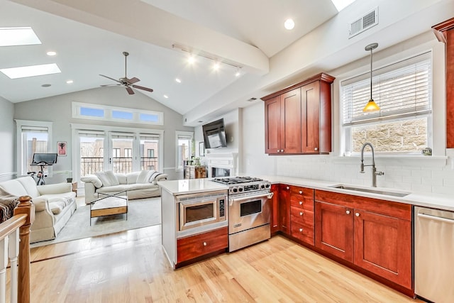 kitchen with sink, a skylight, hanging light fixtures, light wood-type flooring, and appliances with stainless steel finishes