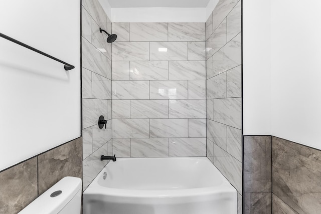 bathroom with tiled shower / bath combo, tile walls, and toilet