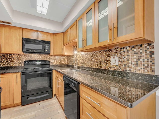 kitchen with tasteful backsplash, sink, dark stone countertops, and black appliances