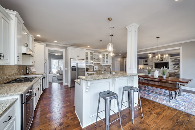 kitchen with appliances with stainless steel finishes, glass insert cabinets, ornamental molding, and dark wood-style floors