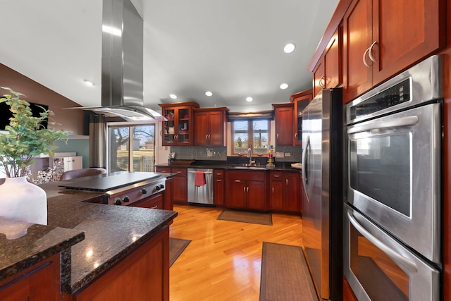 kitchen featuring stainless steel appliances, light hardwood / wood-style floors, island exhaust hood, decorative backsplash, and dark stone counters