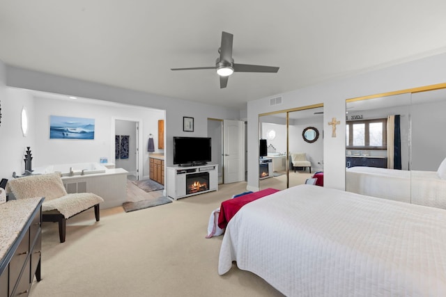 carpeted bedroom featuring two closets, ceiling fan, and ensuite bath