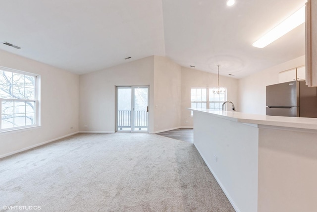 unfurnished living room with lofted ceiling, dark carpet, a wealth of natural light, and a chandelier