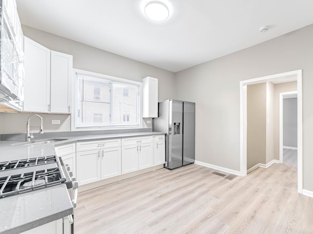 kitchen with white cabinetry, sink, light stone counters, stainless steel fridge with ice dispenser, and light wood-type flooring