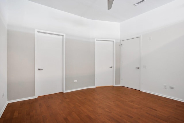 unfurnished bedroom with dark hardwood / wood-style flooring, two closets, and ceiling fan