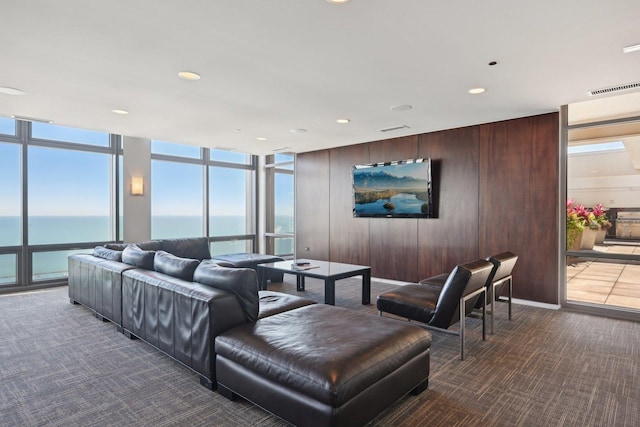 living room with wooden walls, carpet, expansive windows, and a water view