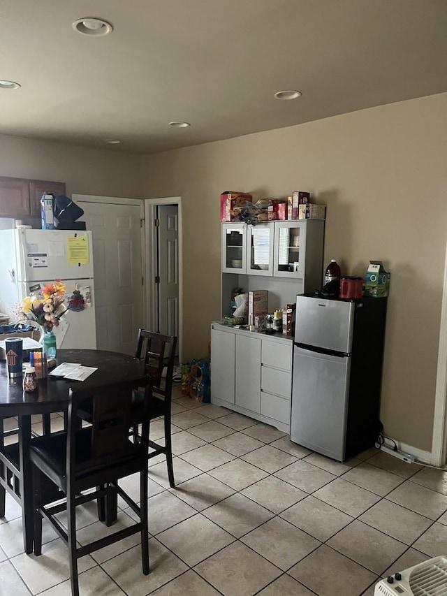 kitchen featuring white refrigerator, white cabinets, light tile patterned floors, and stainless steel refrigerator