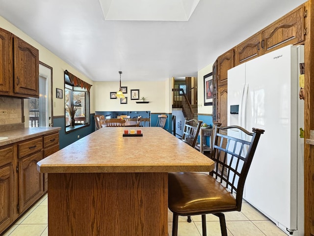 kitchen featuring a center island, light tile patterned floors, hanging light fixtures, and white fridge with ice dispenser