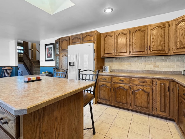 kitchen featuring light tile patterned flooring, tasteful backsplash, white refrigerator with ice dispenser, and a breakfast bar area