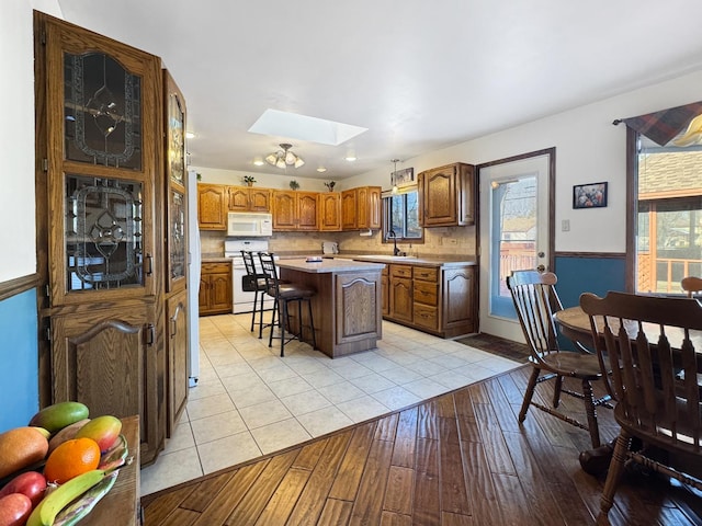 kitchen featuring white appliances, a breakfast bar, a skylight, a center island, and light wood-type flooring